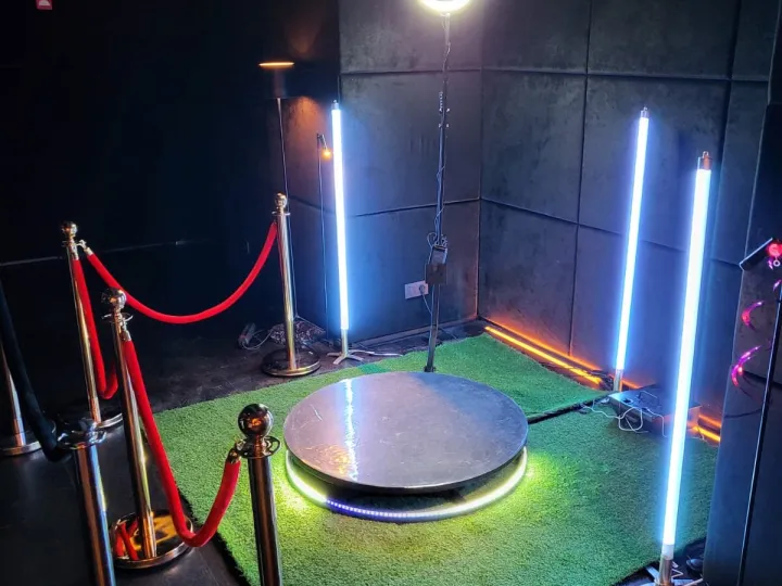 Plataforma 360 con columnas de luz y moqueta verde en una sala oscura